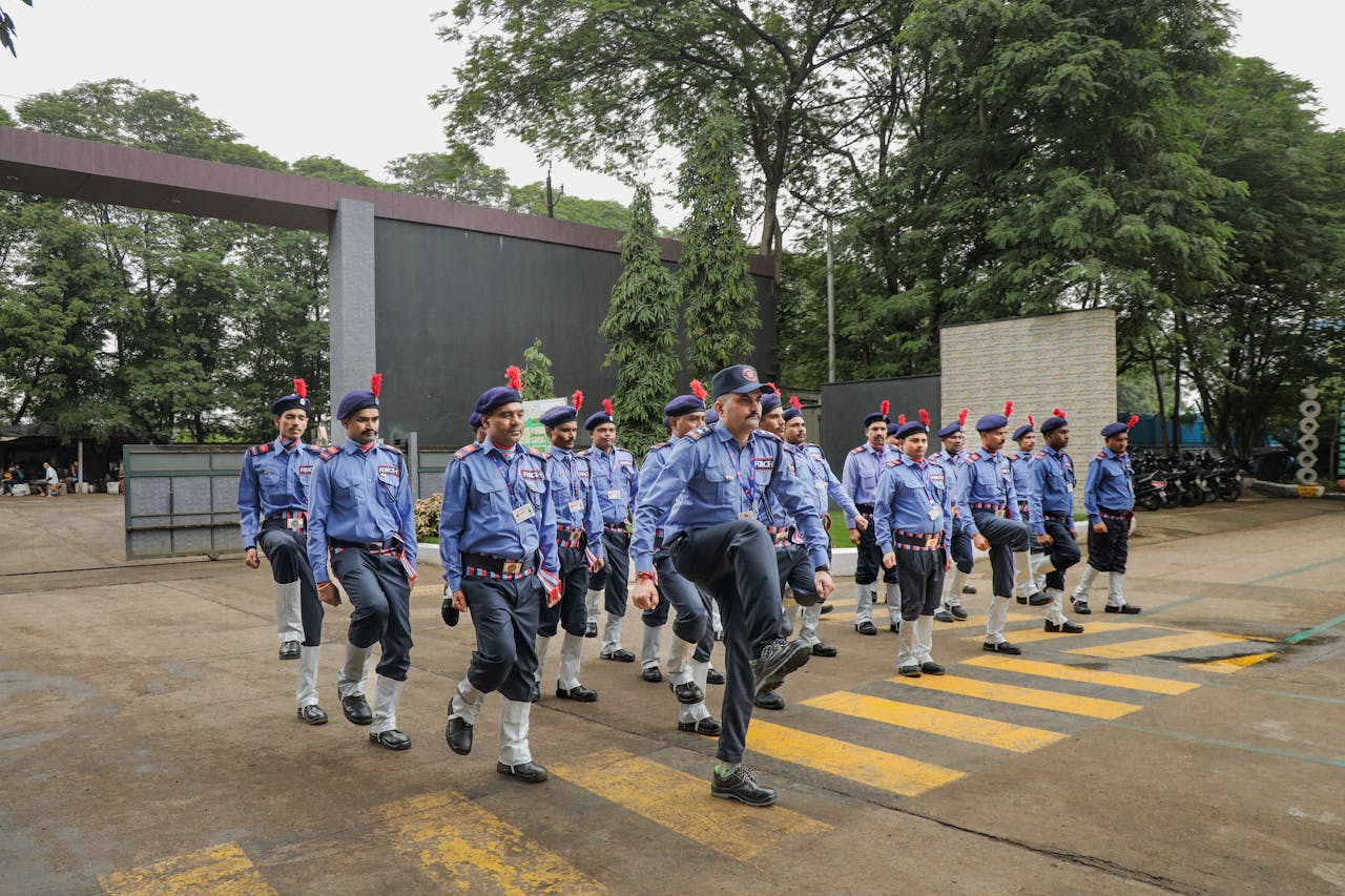 A group of Indian police cadets perform a synchronized march outdoors under cloudy skies.