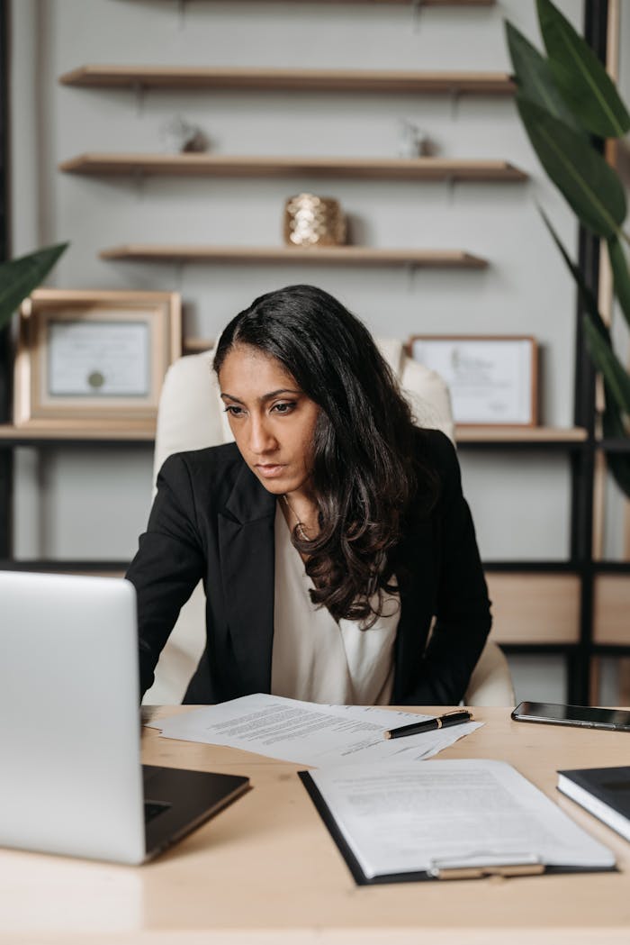 A professional businesswoman in a black suit focused on work at her office desk.