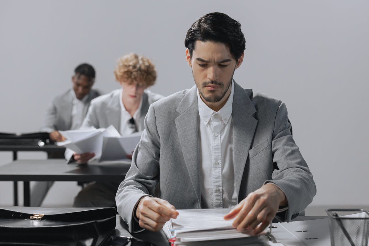 Serious businessmen in gray suits reviewing documents in an office environment.